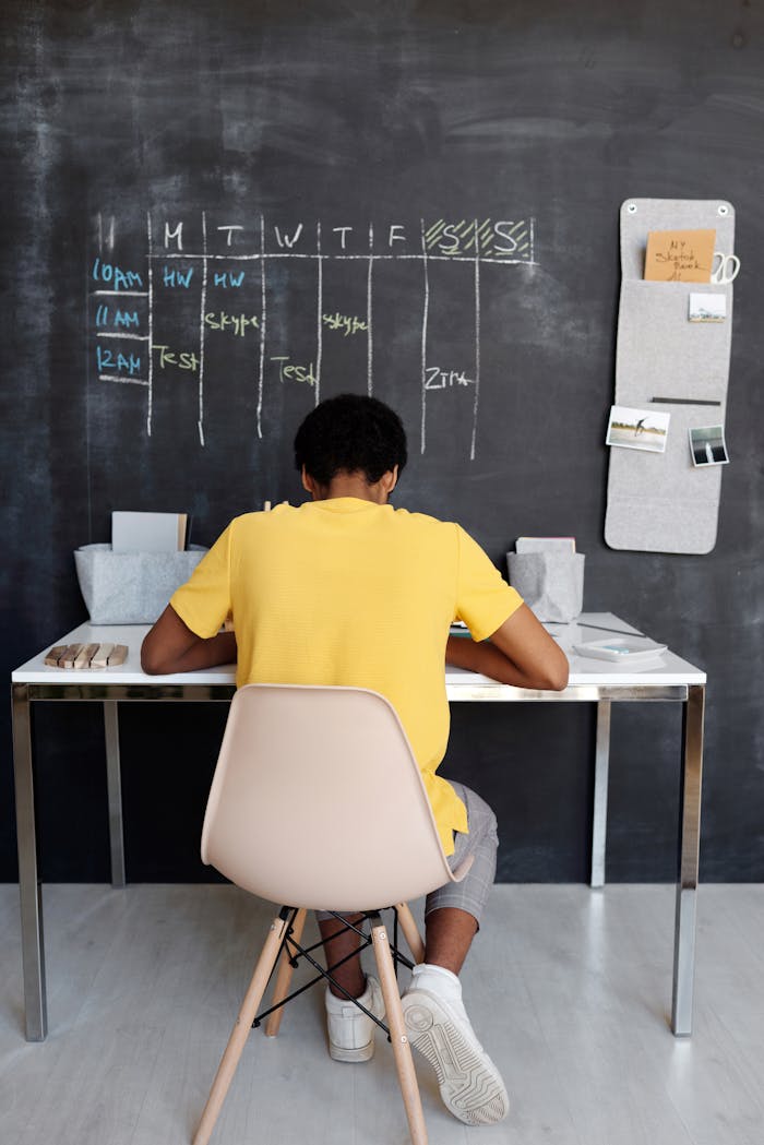 services-01 A teenager focuses on studying at a desk, with a blackboard displaying a schedule in the background.
